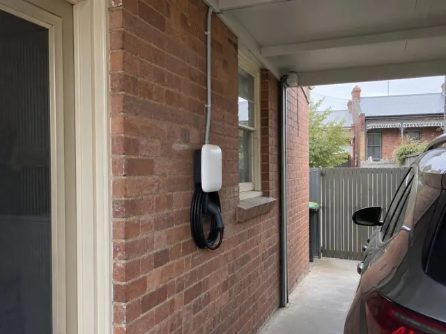 Wall-mounted EV charger on a red brick exterior wall under a carport beside a driveway in Bondi
