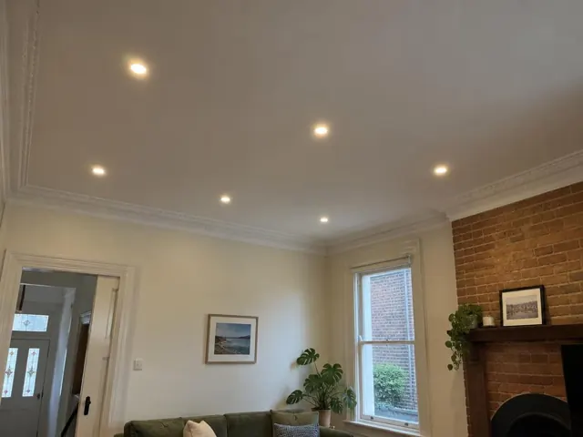 Ceiling downlights in a living room with brick fireplace, cream walls and window trim in Randwick