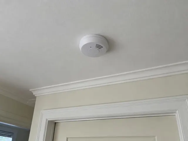 Ceiling smoke alarm above a doorway in a painted interior with cornice in Bronte
